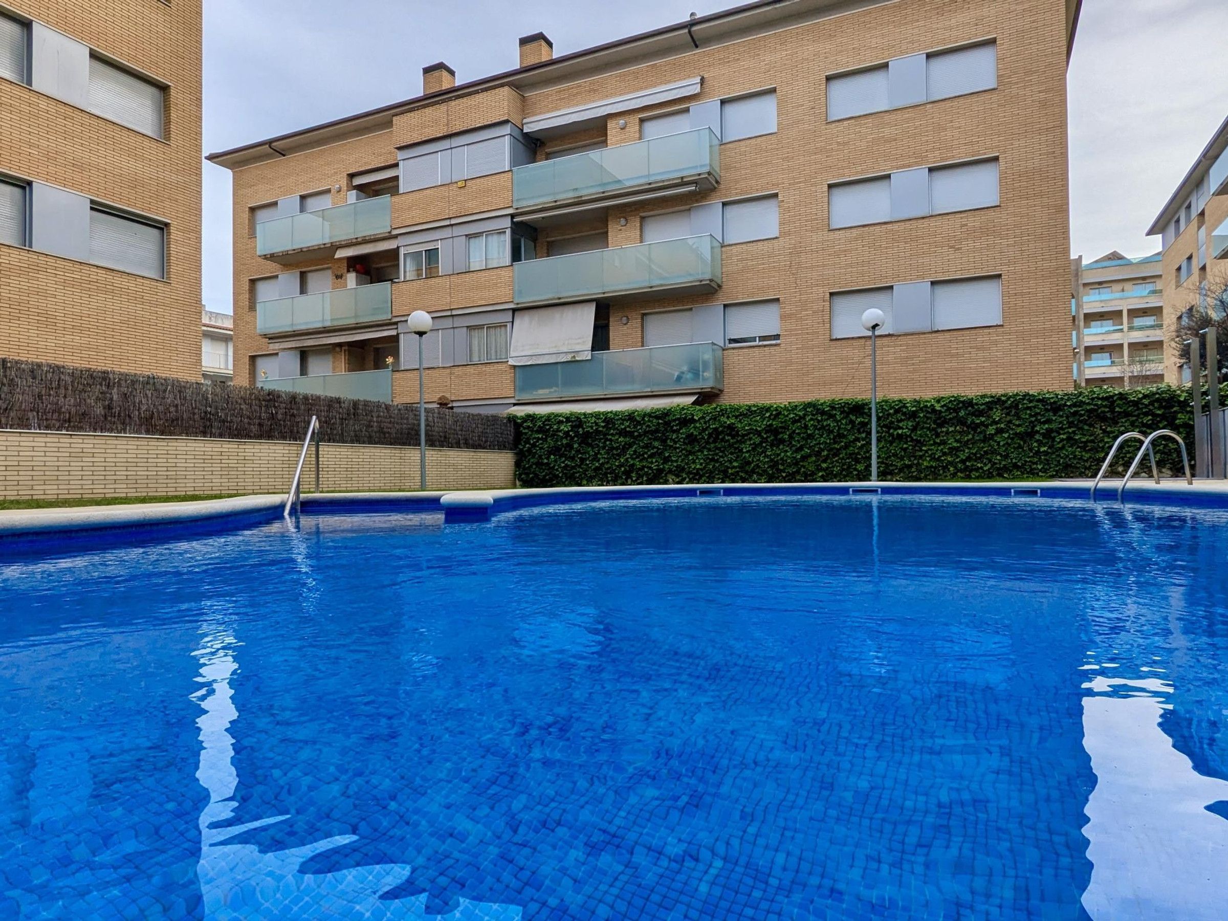 Une piscine à l’eau d’un bleu limpide, entourée d’un bâtiment en briques doté de nombreux balcons.
