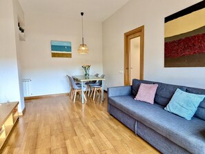 Un salon moderne avec un canapé gris, une table à manger avec des chaises, un luminaire suspendu et des œuvres d’art accrochées aux murs.