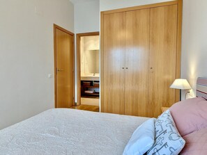 Ein Schlafzimmer mit einem Bett, einem Kleiderschrank und einem durchgehenden Türbogen sichtbarem Badezimmer.