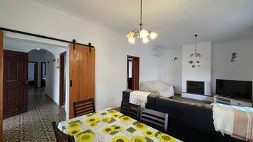 A room with a bed, a TV, a fireplace, and a dining table with a sunflower tablecloth.