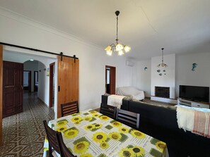 Ein Zimmer mit einem Bett, einem Fernseher, einem Kamin und einem Esstisch mit einer Sonnenblumen Tischdecke.