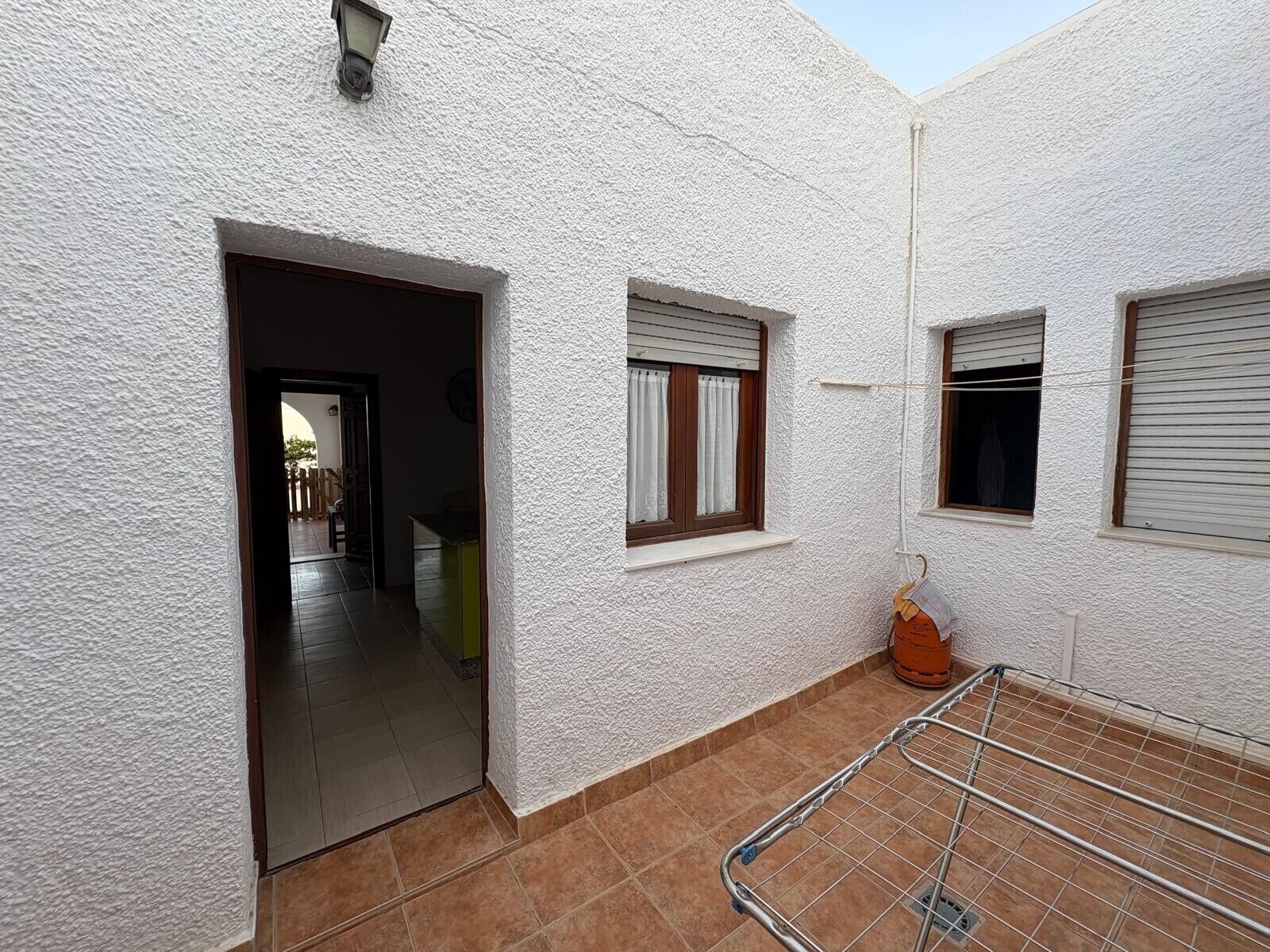 A white-walled building with a tiled patio, a laundry rack, and a door leading to an interior space.