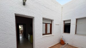 Un edificio dalle pareti bianche con un patio piastrellato, uno stendibiancheria e una porta che dà su un ambiente interno.