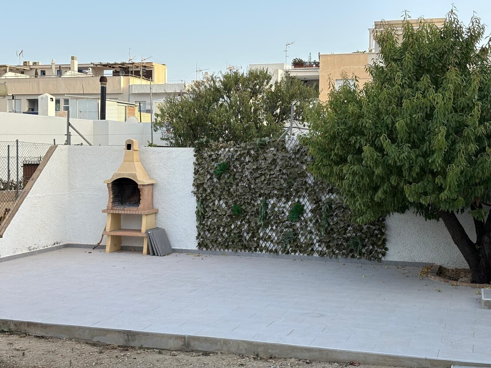 A rooftop with a brick oven, a white wall, and a tree.