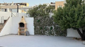 A rooftop with a brick oven, a white wall, and a tree.