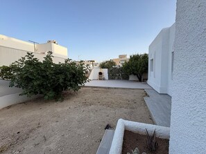 Um pátio com um pequeno jardim, uma parede branca e um edifício ao fundo.