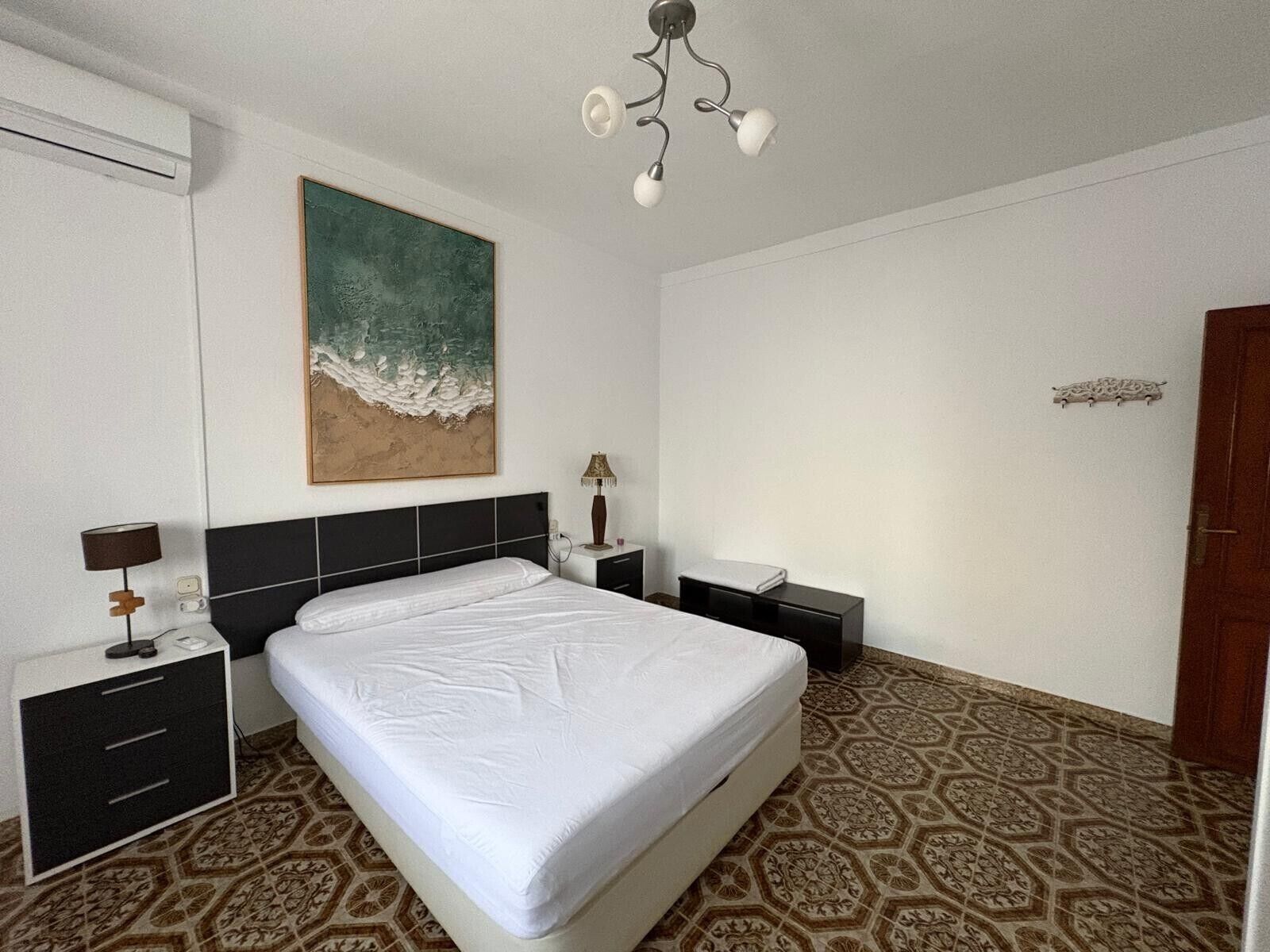 A hotel room with a bed, bedside tables, a lamp, a painting, and a patterned floor.