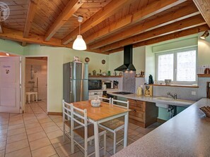 Eine Küche mit Holzbalken, einem Edelstahl-Kühlschrank, einem Esstisch mit Stühlen und einem Fenster mit Aussicht.