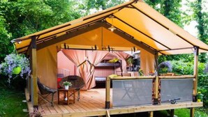 Uma tenda com um deck de madeira, uma mesa, cadeiras e uma pequena área de jardim.