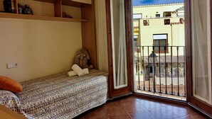 Ein Zimmer mit einem Bett, einem kleinen Tisch, einer Ablage mit Gläsern und Blick ins Freie.