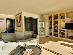 Ein Wohnzimmer mit einer Couch, einem Couchtisch mit Dekoration, einem Bücherregal und einem Fernseher.