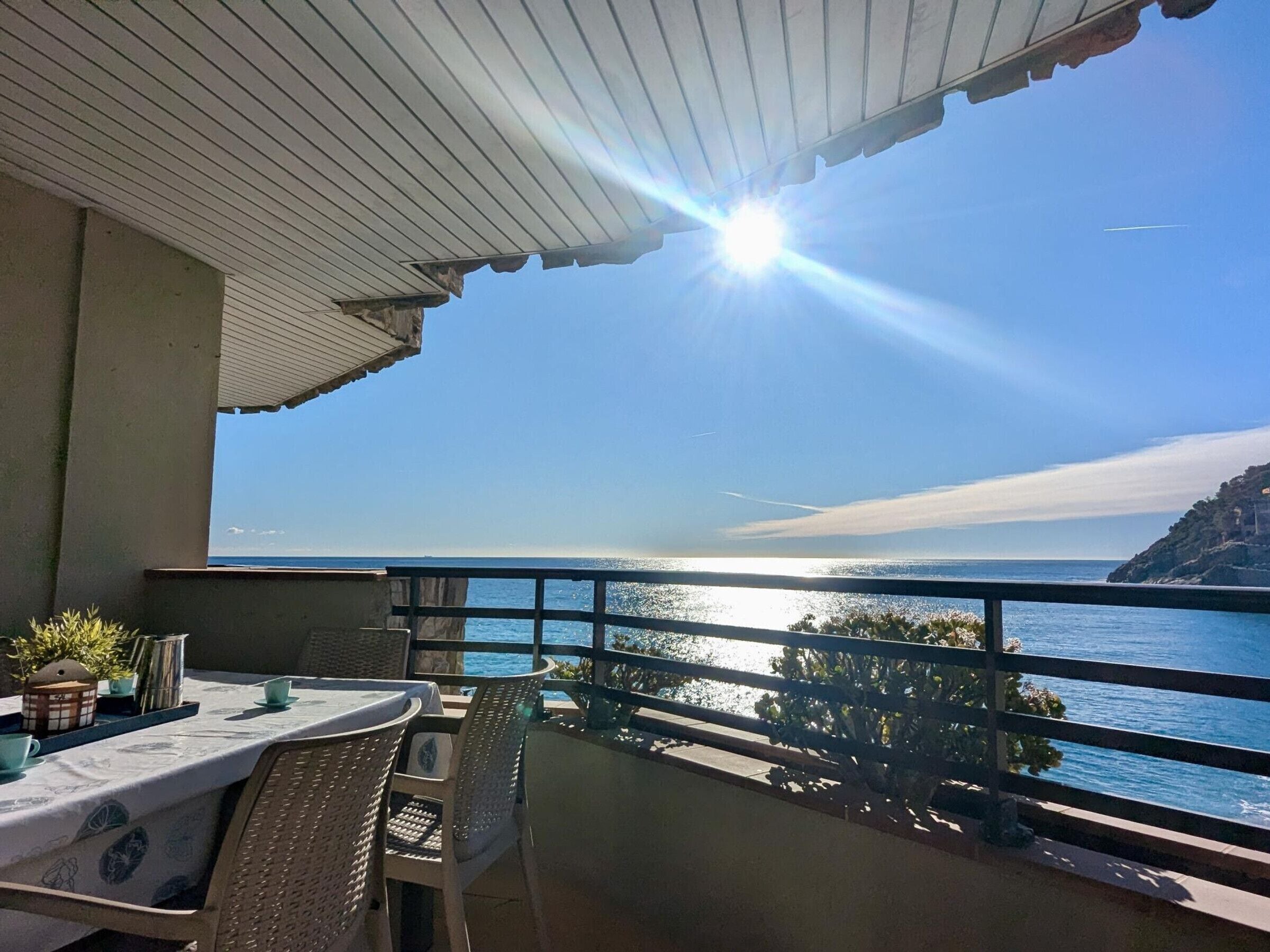 Ein Balkon mit Tisch und Stühlen, der Blick auf die Küste und einen klaren Himmel bietet.