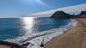 Una spiaggia con cielo sereno, il sole che si riflette sull'acqua e una scogliera con edifici.