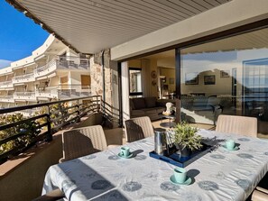 A balcony with a table set for two, a potted plant, and a view of a multi-story building. - Family apartment with sea view - 6 guests (Tossa de Mar)