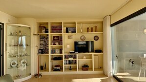 Un soggiorno con una vetrina a vetro, una televisione e una porta scorrevole in vetro che dà su un balcone.