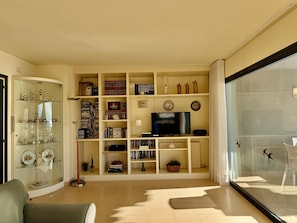 Ein Wohnzimmer mit einer Vitrine aus Glas, einem Fernseher und einer Glastür, die auf einen Balkon führt.