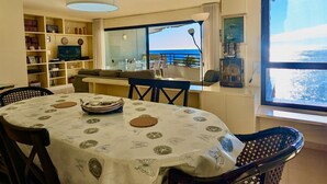 Zona pranzo con tavolo apparecchiato per due, un divano e una televisione sullo sfondo.