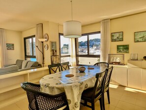 Ein Essbereich mit Tisch für zwei Personen, einer Couch und Blick auf eine Küstenlandschaft durch große Fenster.