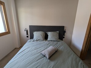 Ein Schlafzimmer mit einem Bett, zwei Wandnischen als Nachttische, einem Fenster und einer Tür.