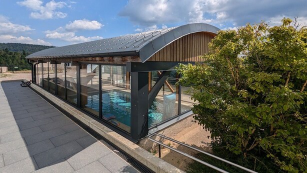 Ein moderner Pool im Freien mit Glasveranda, umgeben von einer gepflasterten Fläche und einer Holzkonstruktion.