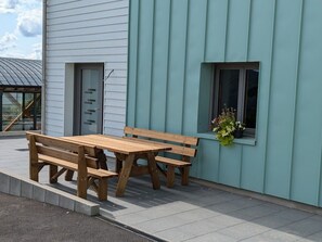 A wooden bench and table set up on a patio next to a building with a window and a door. - Mountain lodge with valley view (Le Val-d'Ajol)