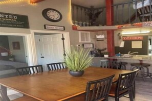 A dining area with a wooden table, chairs, and a potted plant. There is a kitchen area with a sign that reads 'TCHEN'. - Lazy Duck Cottages The Whole Flock In One Booking (Duck Creek Village)