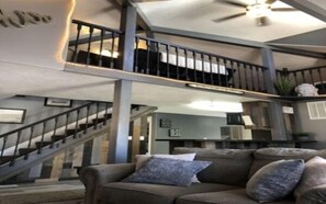Un espacio habitable de varios niveles con una escalera, un sofá con almohadones y un ventilador de techo.