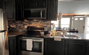 A modern kitchen with dark cabinetry, stainless steel appliances, and a tiled backsplash. - Lazy Duck Cottages The Whole Flock In One Booking (Duck Creek Village)