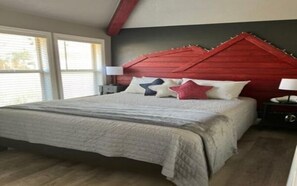 A bedroom with a bed, a nightstand, and a window. - Lazy Duck Cottages The Whole Flock In One Booking (Duck Creek Village)
