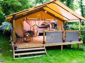 Ein Zelt mit einer Holzterrasse, einem Tisch, Stühlen und einer kleinen Gartenanlage.