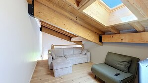 Ein Loft-Zimmer mit schrägem Dach, Holzbalken, einer Couch und einem kleinen Tisch.