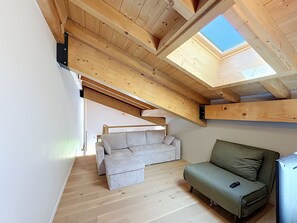 Ein Loft-Zimmer mit schrägem Dach, Holzbalken, einer Couch und einem kleinen Tisch.