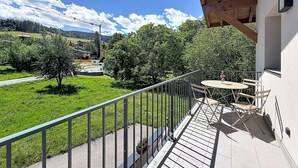 Ein Balkon mit Tisch und Stühlen, der auf eine grüne Landschaft mit Bäumen und einen entfernten Blick auf einen Baukran blickt.
