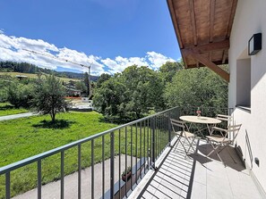 Ein Balkon mit Tisch und Stühlen, der auf eine grüne Landschaft mit Bäumen und einen entfernten Blick auf einen Baukran blickt.