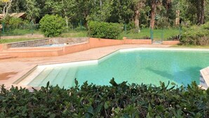 Una piscina con agua cristalina azul, rodeada por un solado de piedra y abundante vegetación.
