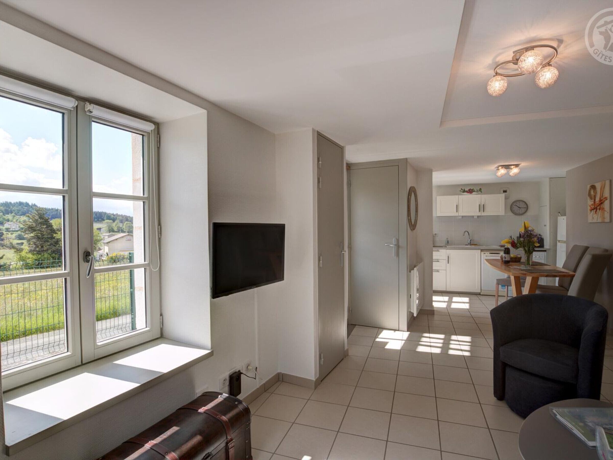A modern apartment with a large window, a flat-screen TV, a dining area, and a kitchen.
