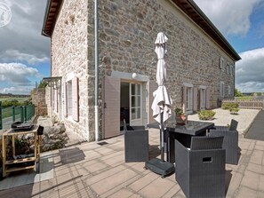 A stone building with a patio area featuring outdoor furniture and a covered table. - Modern lodge in natural surroundings - 4 guests (Usson-en-Forez)