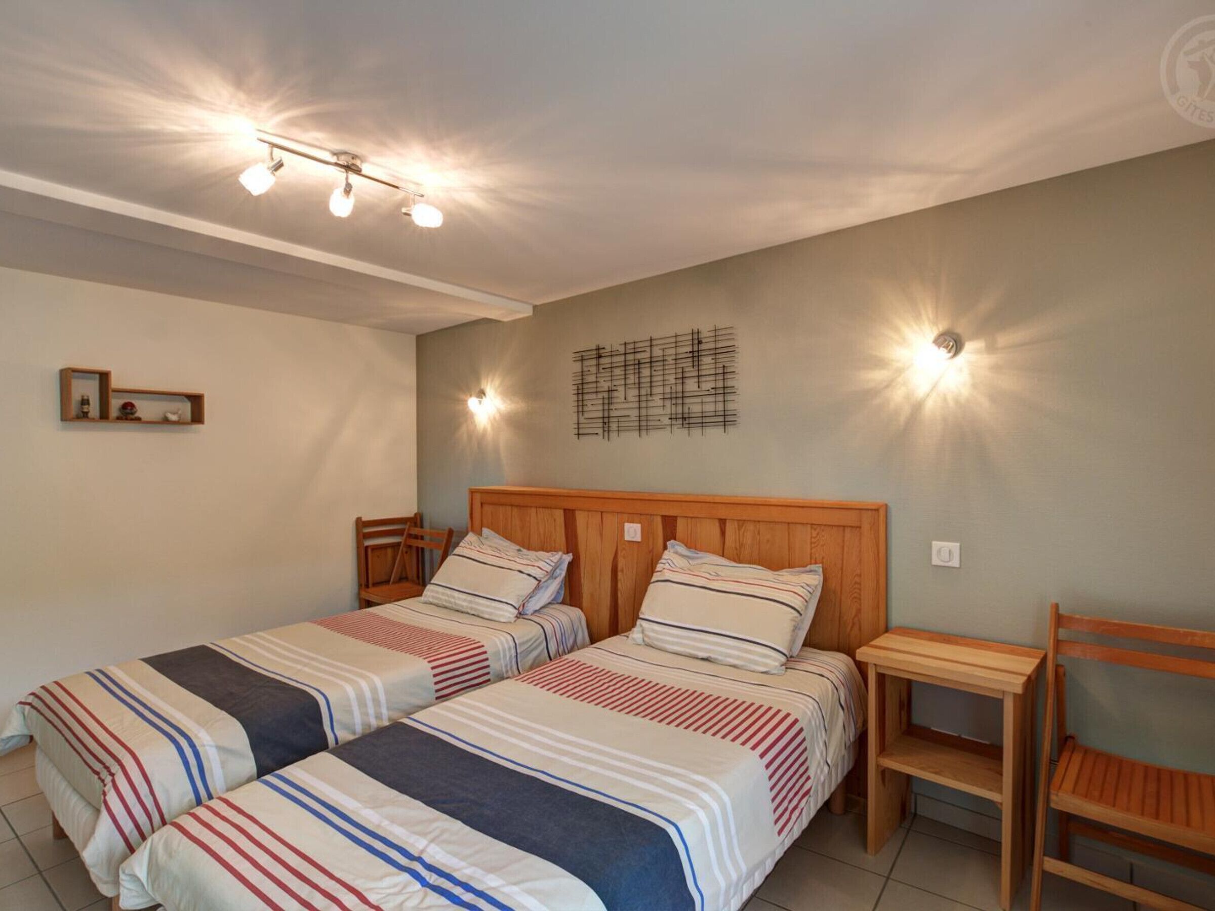 Un dormitorio con dos camas, cabeceros de madera, mesitas de noche e iluminación en la pared.