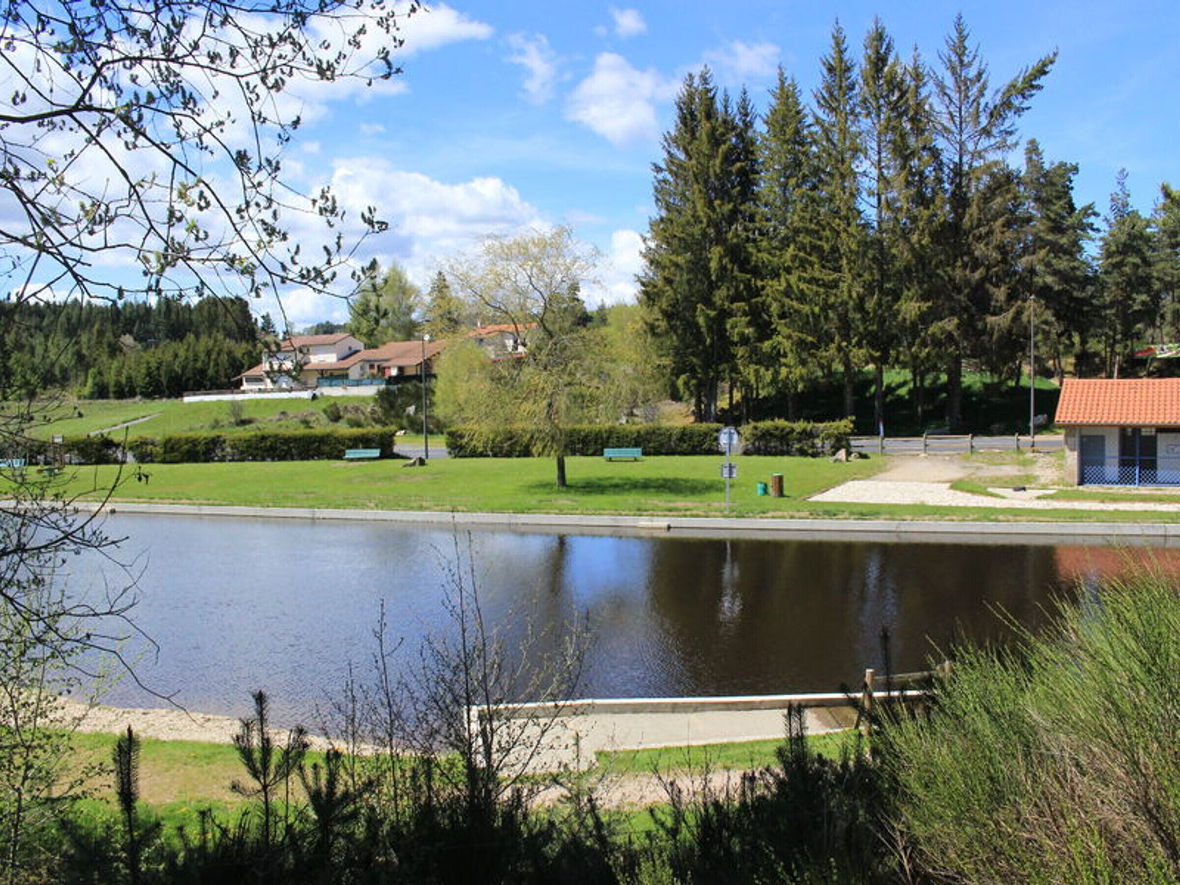 Un parc paisible avec un étang, des bancs et un petit bâtiment.