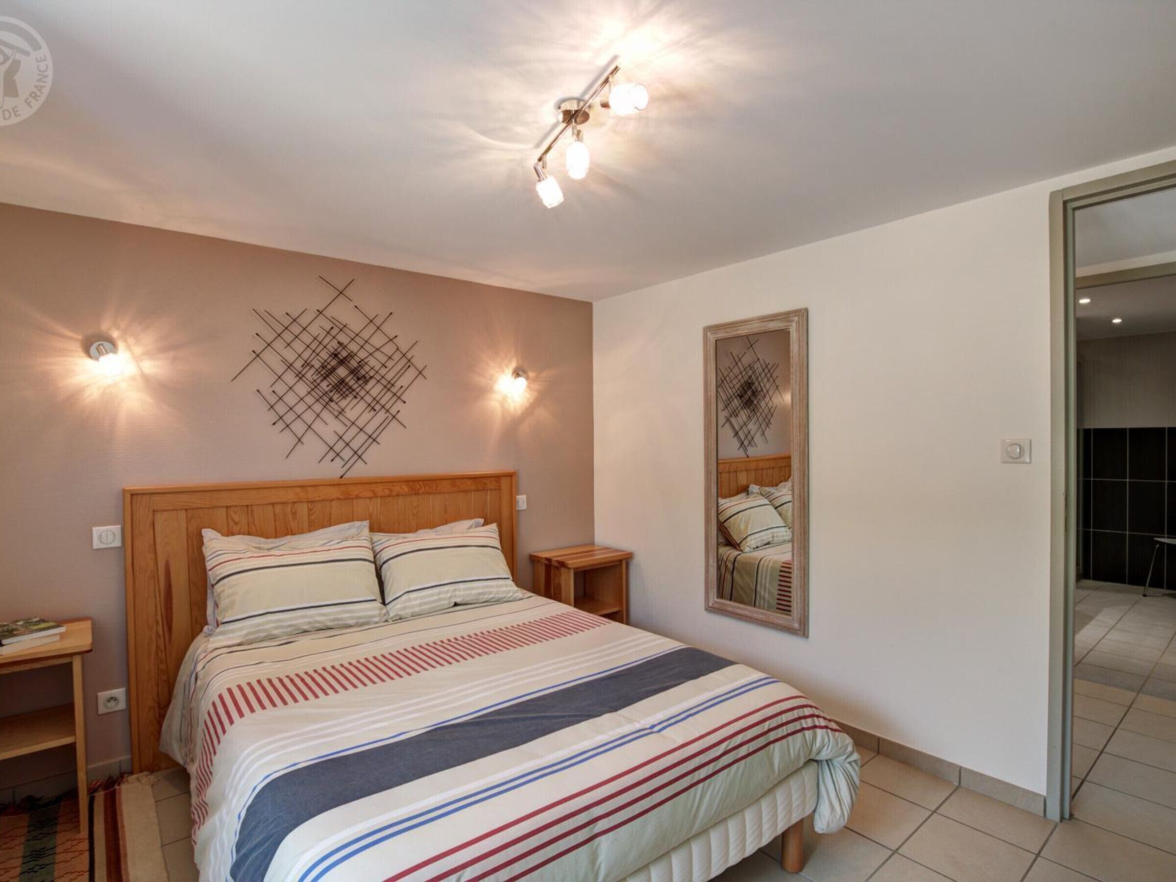 A bedroom with a wooden bed, bedside tables, a wall-mounted light fixture, and a mirror.