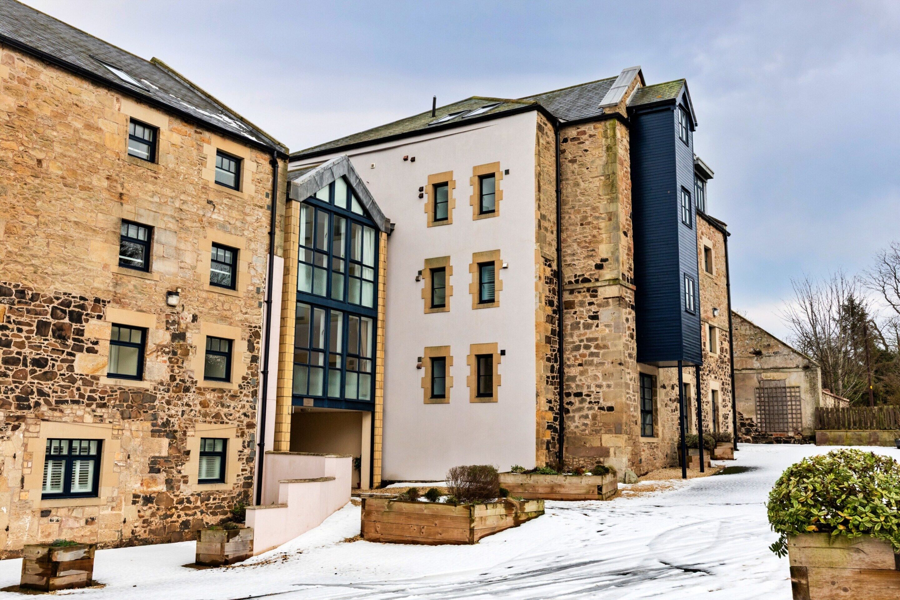 A multi-story building with stone and modern architectural elements, including large windows and a flat roof.