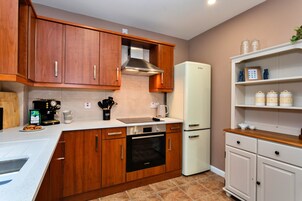 Una cocina compacta con armarios de madera, horno Bosch, refrigerador blanco y una cafetera.
