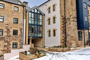 Ein mehrstöckiges Gebäude mit Stein- und moderner Fassade, großen Fenstern und einem mit Schnee bedeckten Untergrund.