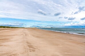 Ein weiter Sandstrand mit sanften Wellen und einem teils bewölkten Himmel.