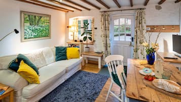 A cozy living room with a sofa, a dining table, a chair, a lamp, and a painting on the wall.