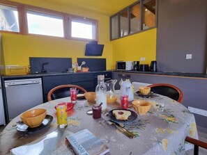 A dining area with a table set for two, a kitchen in the background, and a window providing natural light. - Welcoming gîte, pets allowed - 5 guests (Doizieux)