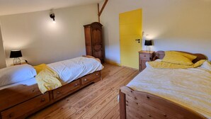 Ein Zimmer mit zwei hölzernen Betten, einem Kleiderschrank, einer gelben Tür und einer Lampe auf einem Nachttisch.