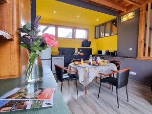 A dining area with a table set for two, a vase with flowers, and a magazine on the table. - Welcoming gîte, pets allowed - 5 guests (Doizieux)