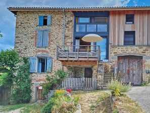 A stone building with a balcony, a wooden door, and a garden with various plants. - Welcoming gîte, pets allowed - 5 guests (Doizieux)