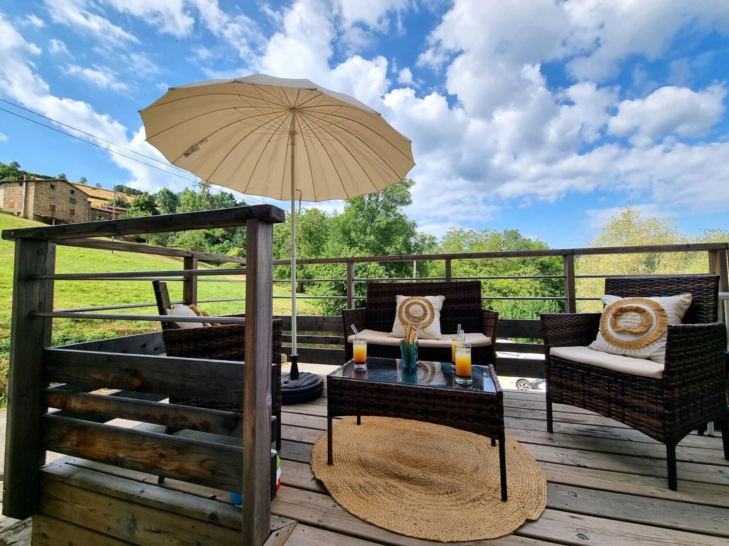 Eine Terrasse im Freien mit Korbmöbeln, einem Tisch mit Getränken und einem großen Sonnenschirm.